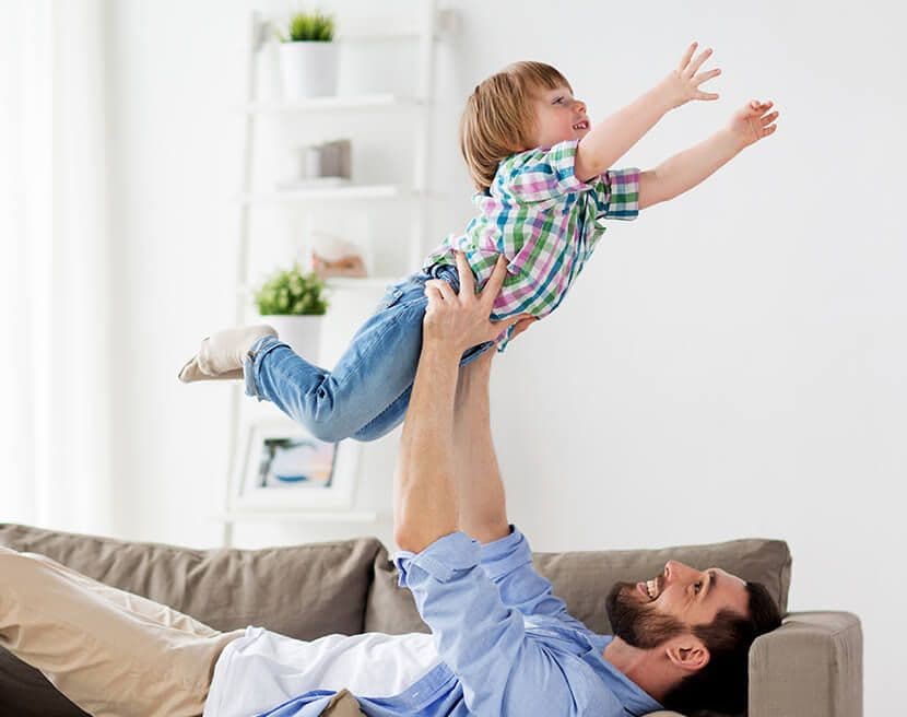 A parent lies on a couch and tosses a child in the air.