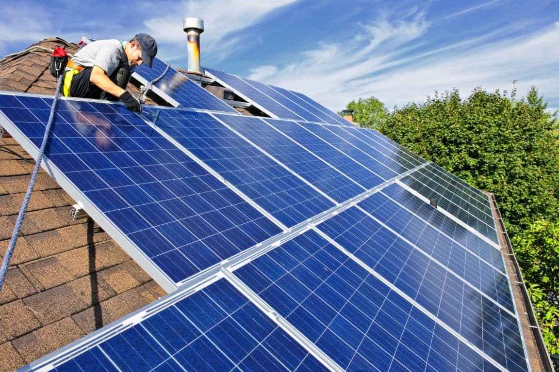 A worker installs solar panels on a roof.