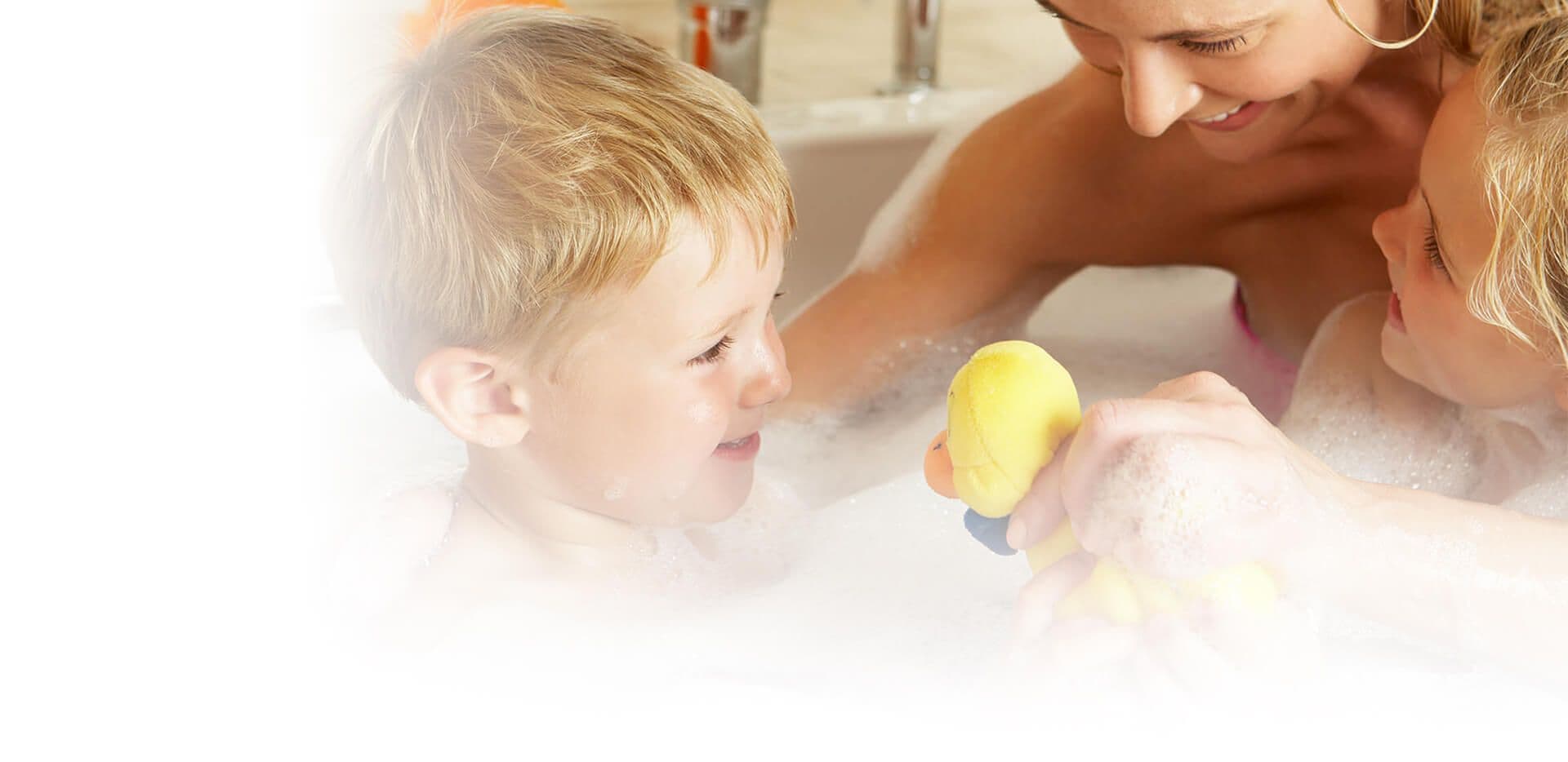 An adult bathes a child in a bath with bubbles.